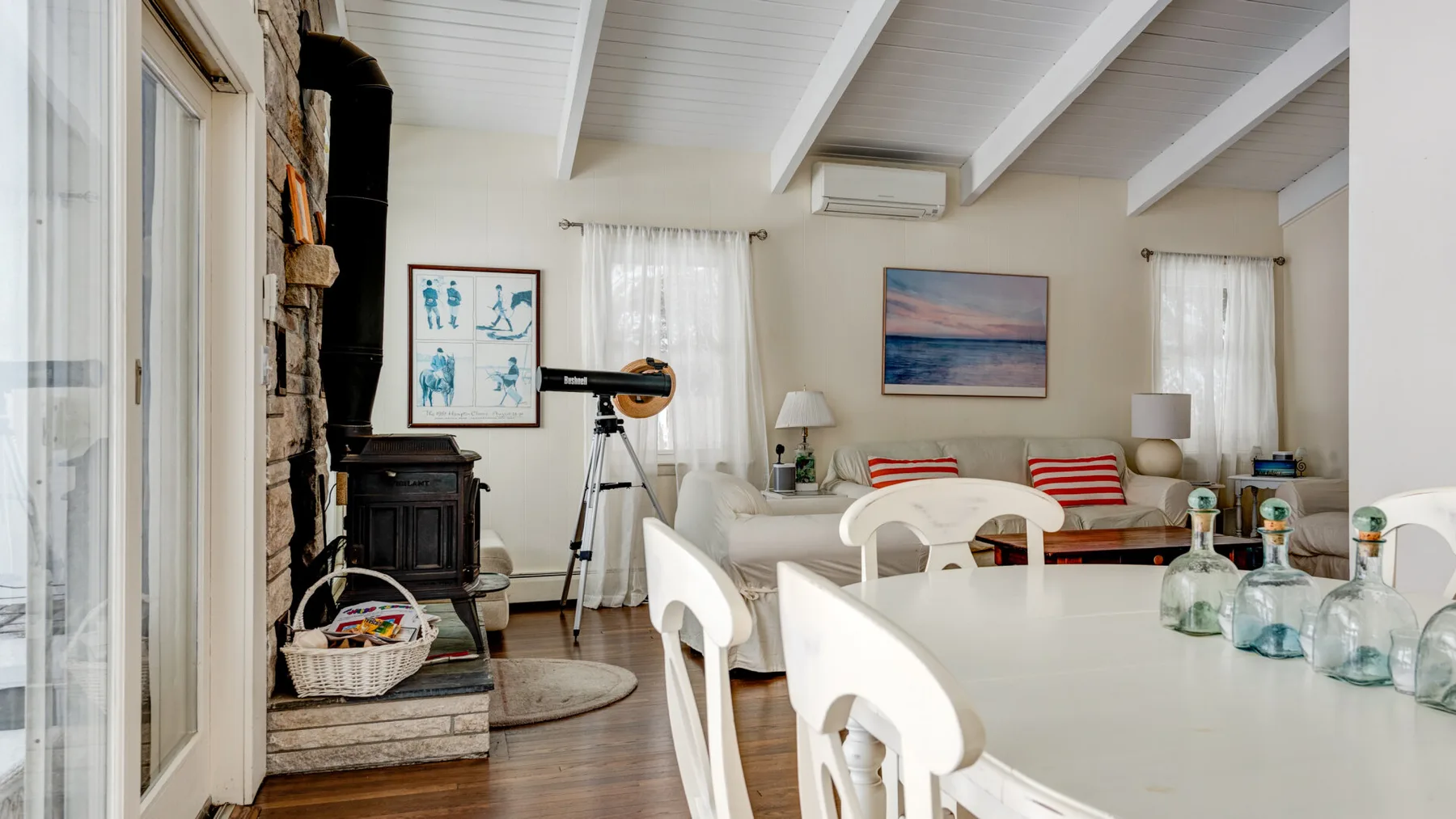 A bright living and dining area with white seating and a telescope.