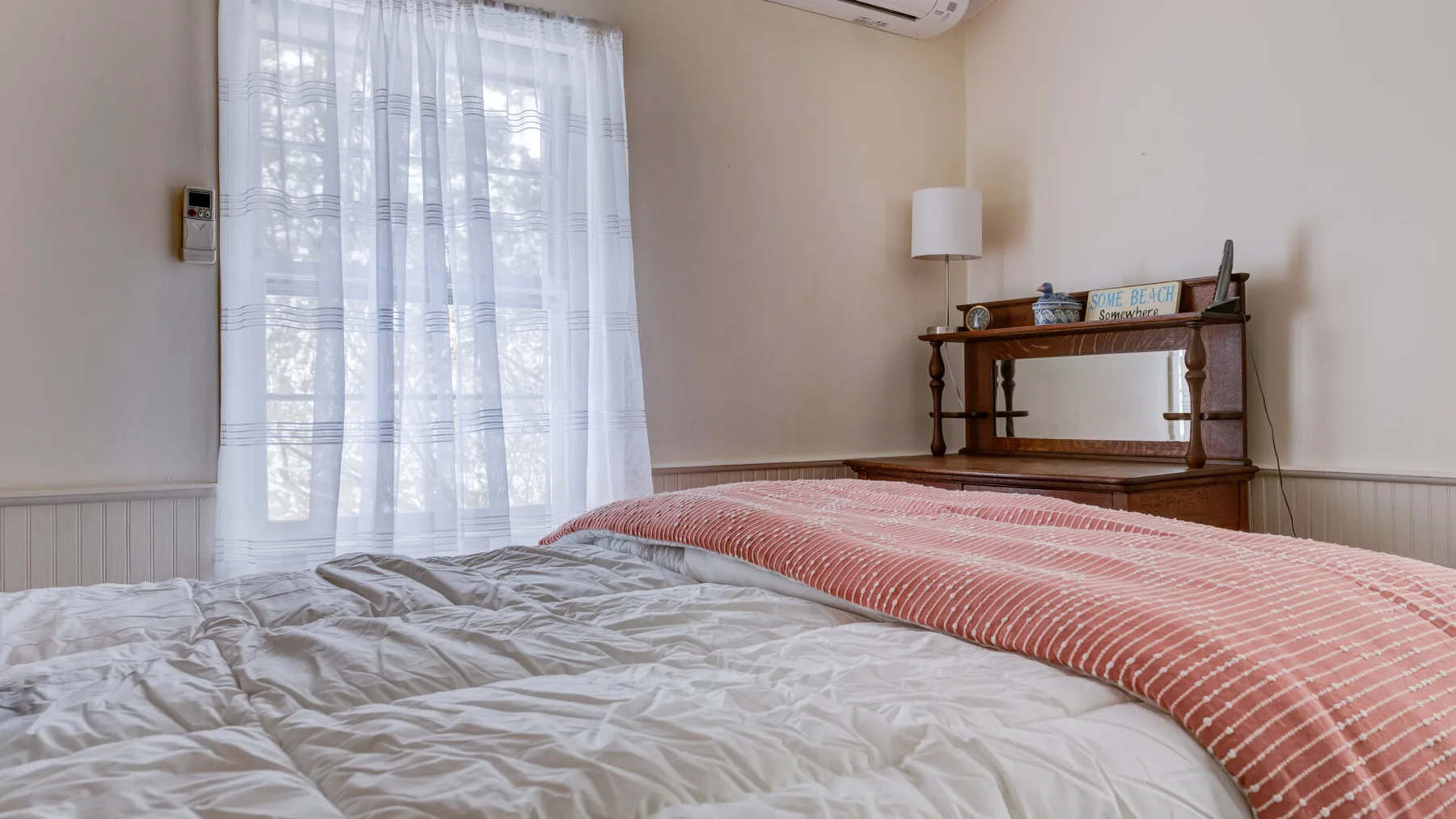 A bedroom with a bed and sheer curtains over the window.