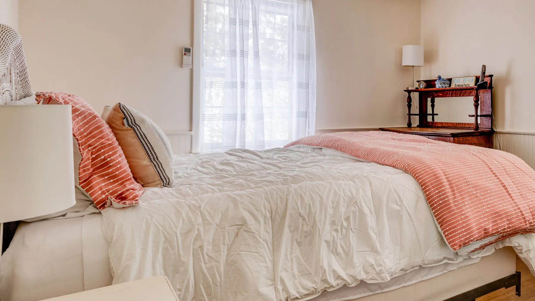 A bedroom with a bed dressed in light bedding and coral-colored accents.