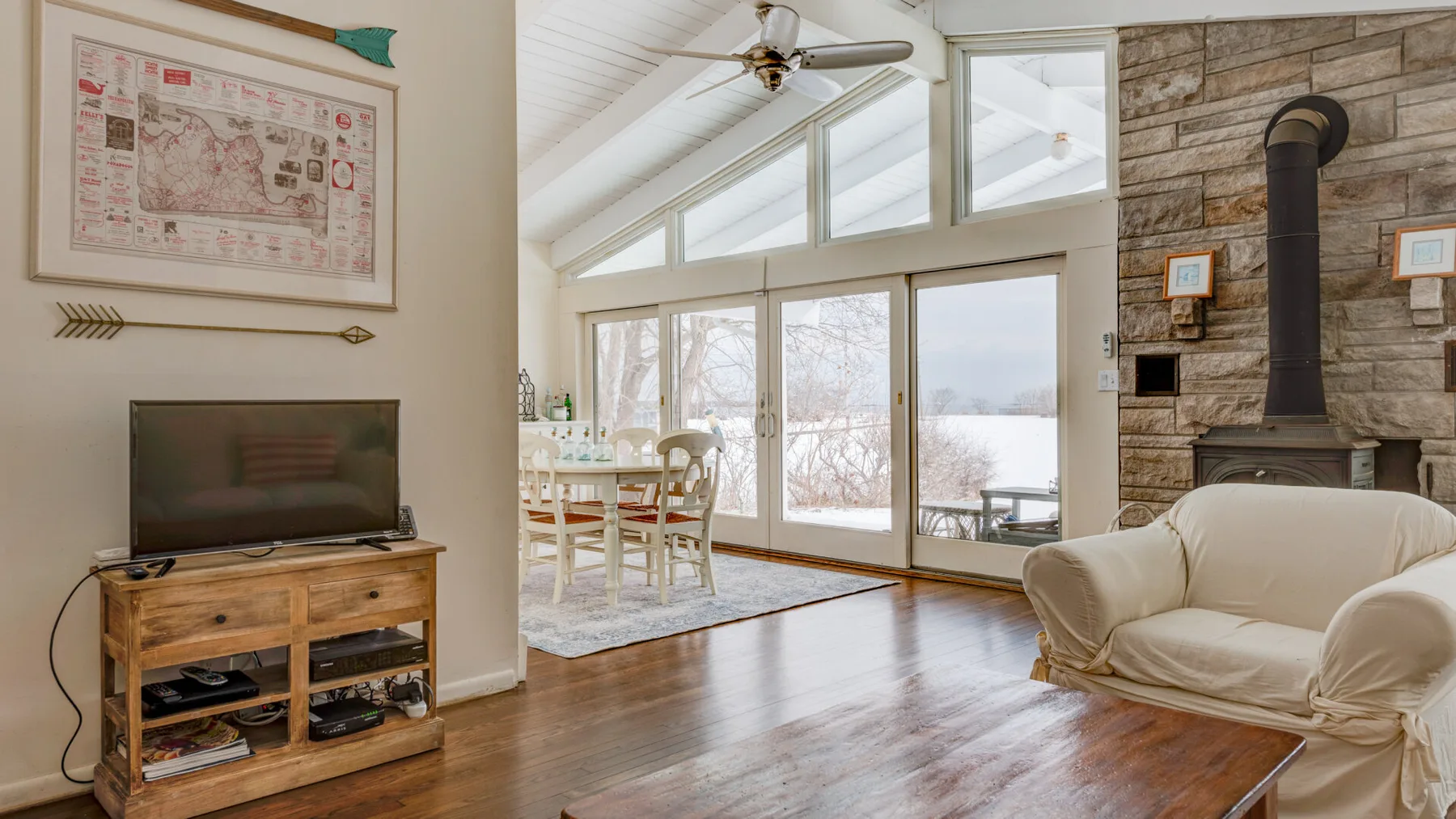A bright living room with large windows, a dining table, and a fireplace.