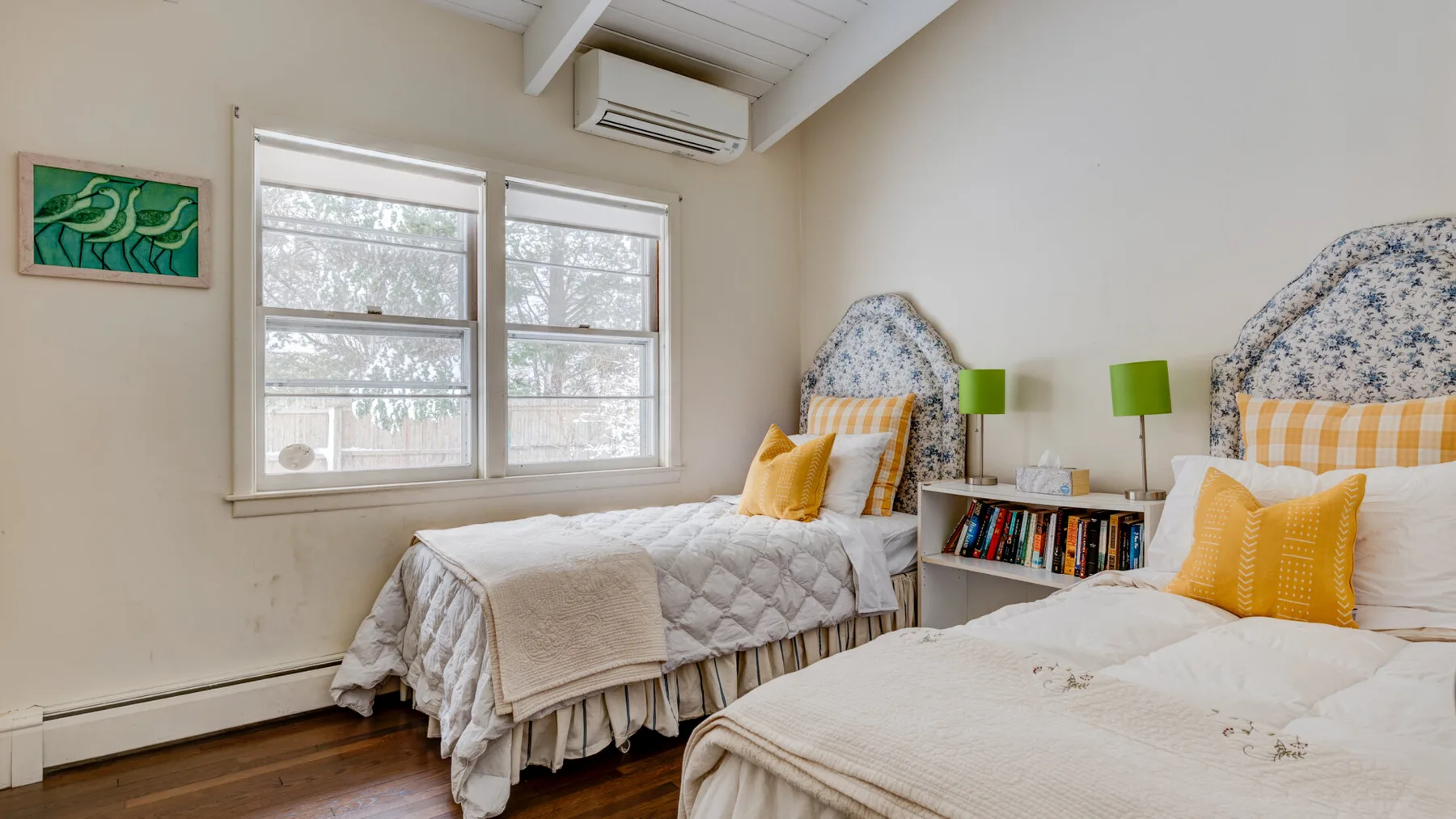 A bedroom with two beds, windows, and a small bookshelf.