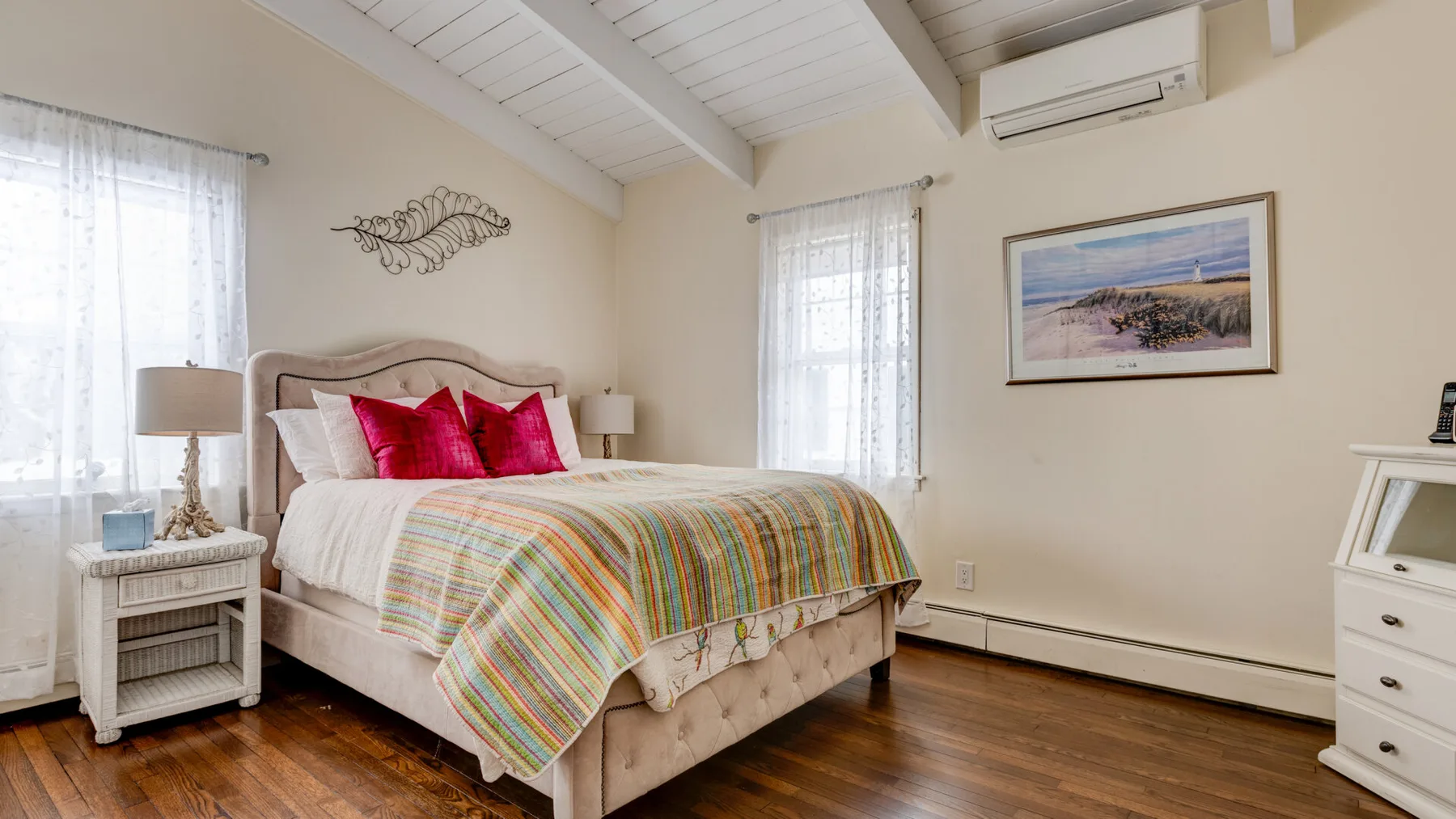 A bright bedroom with a bed covered by a colorful striped quilt.