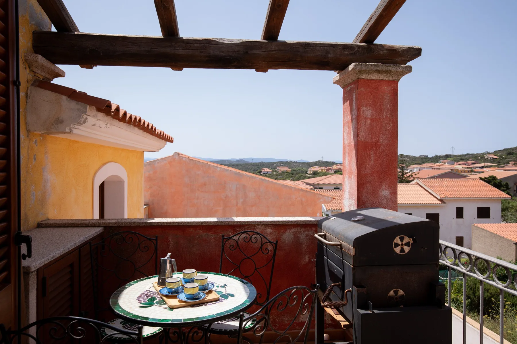 A rooftop terrace with a small table, seating, and a built-in grill overlooks nearby rooftops.