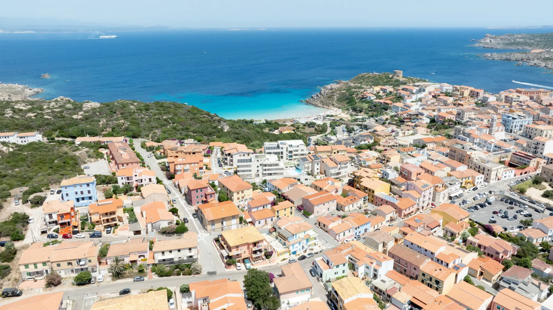 Aerial view of a coastal town beside a turquoise bay and the open sea.