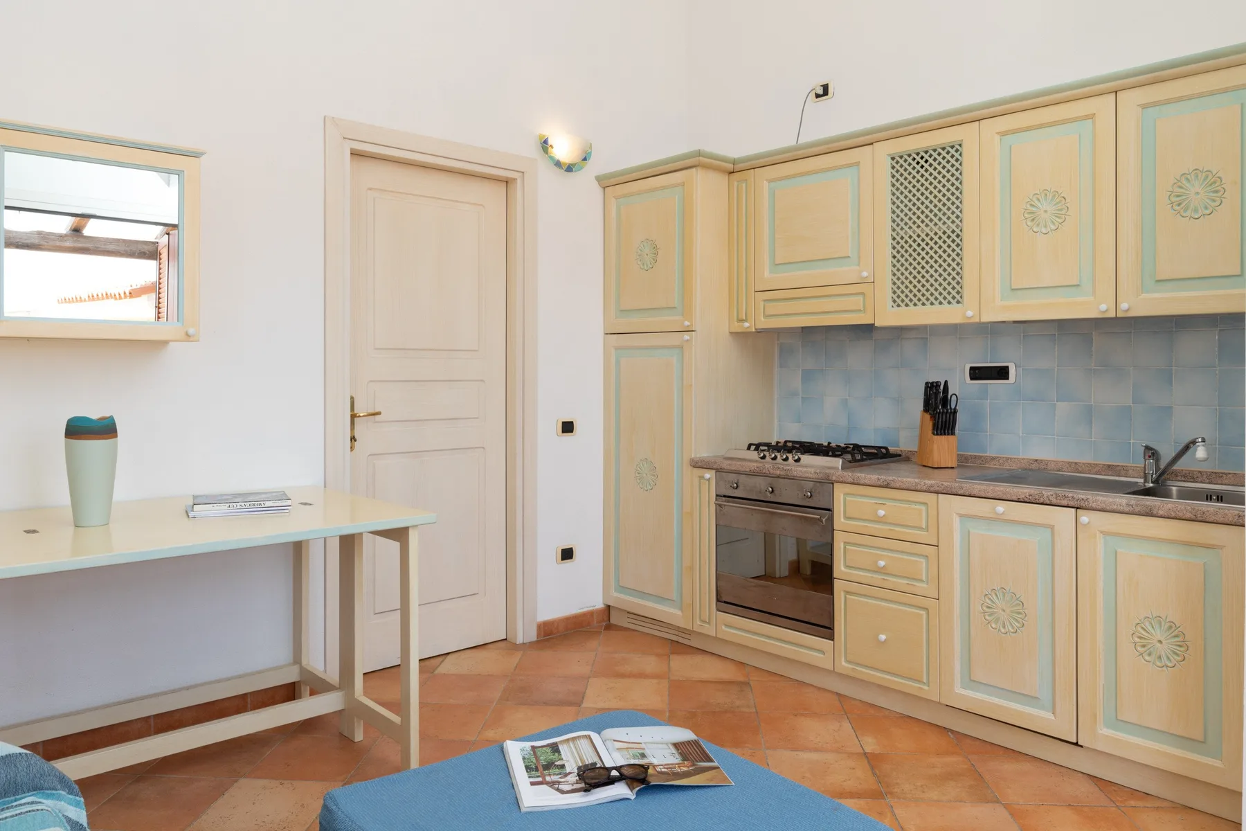 A kitchen with pale cabinets, a stove, and a small table.