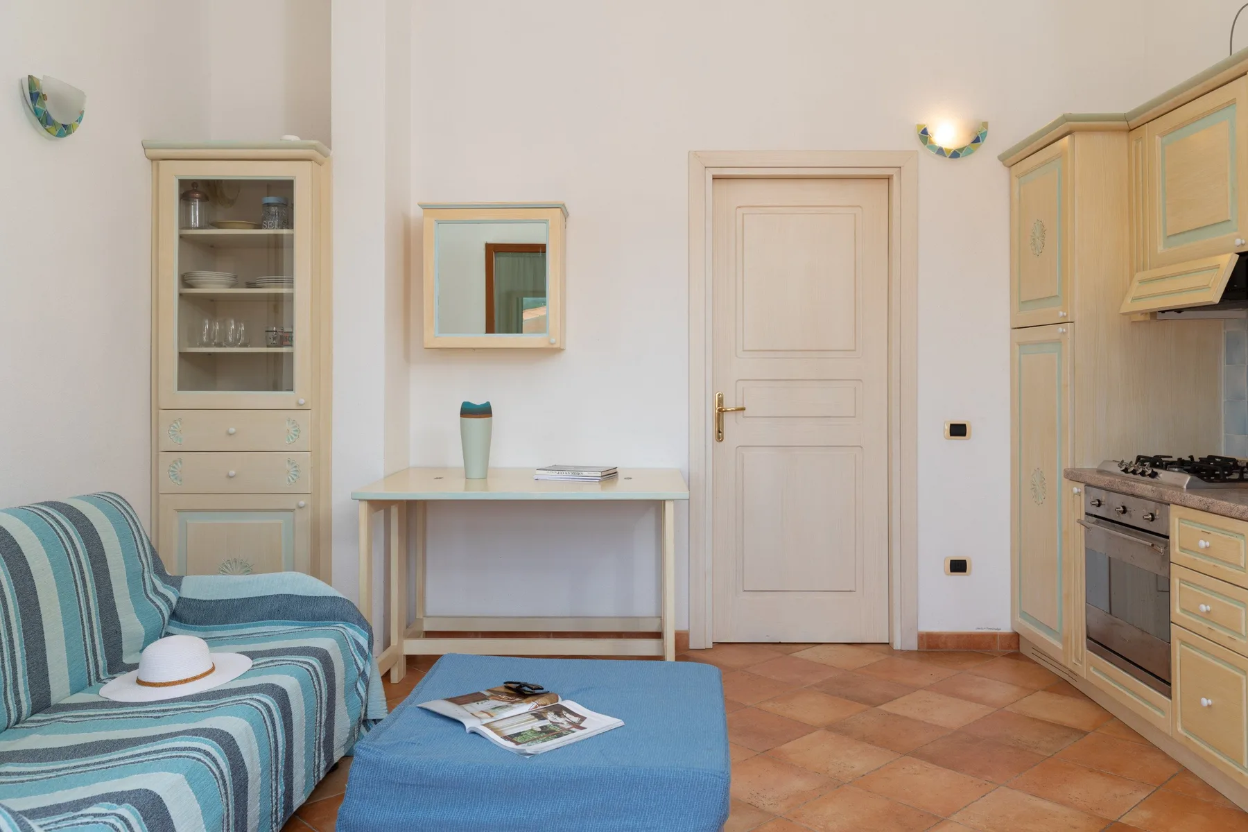 A furnished room with a striped sofa, a small table, and a kitchen area.