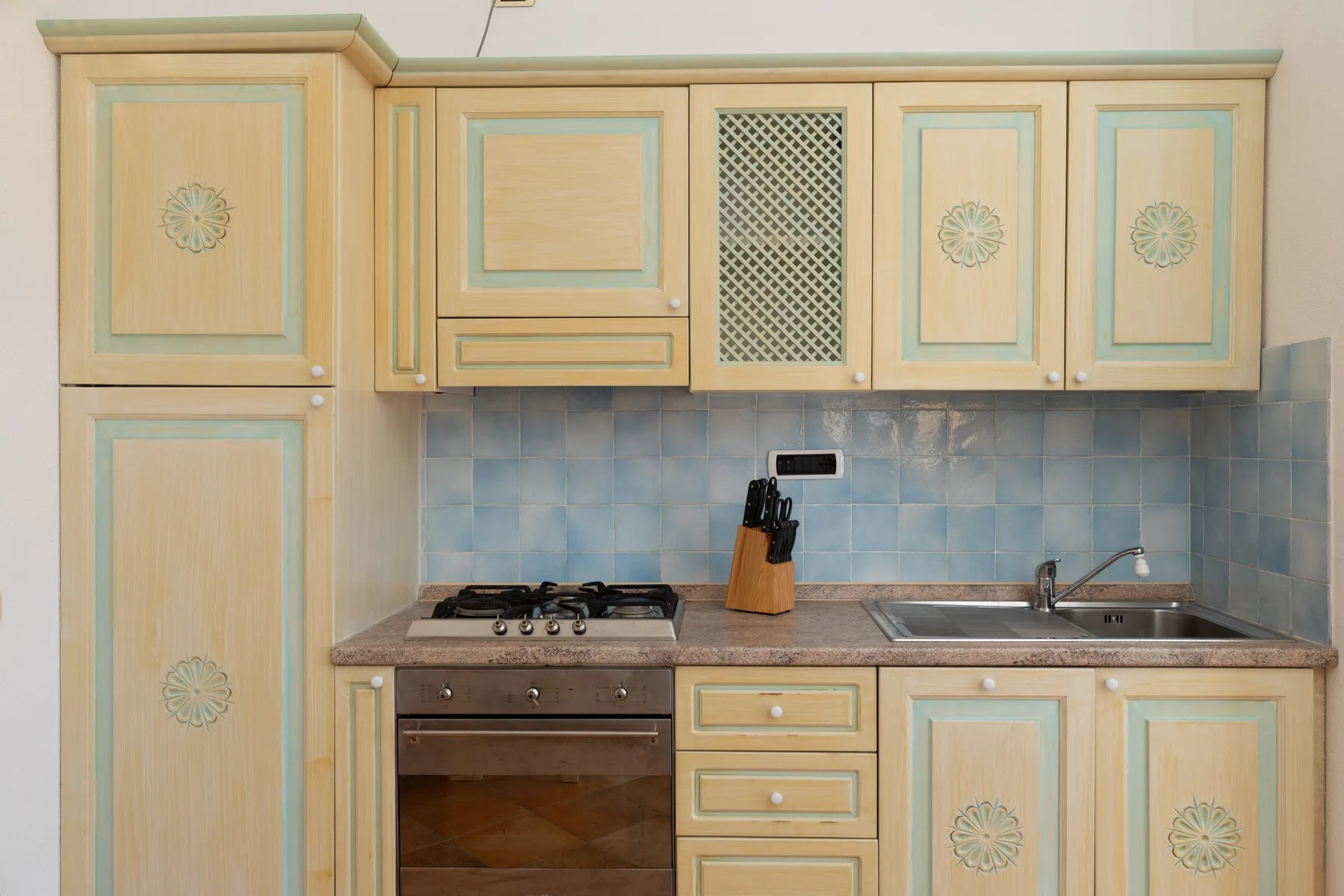 A kitchen with pale wood cabinetry, a cooktop, and a sink.
