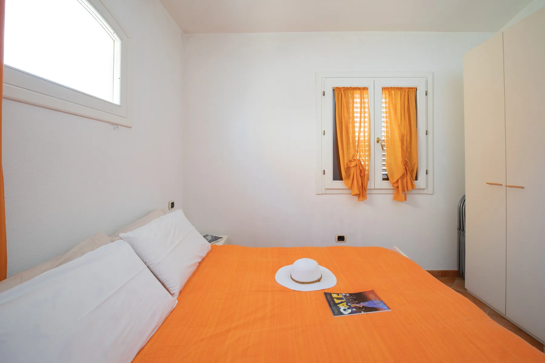 A bedroom with an orange bedspread and orange curtains.