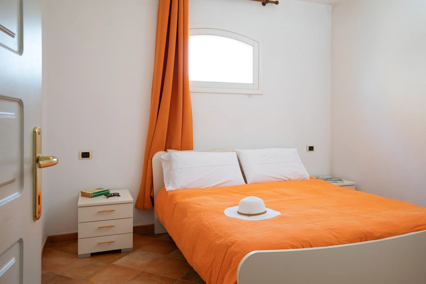 A bedroom with an orange-covered bed and a small window above it.