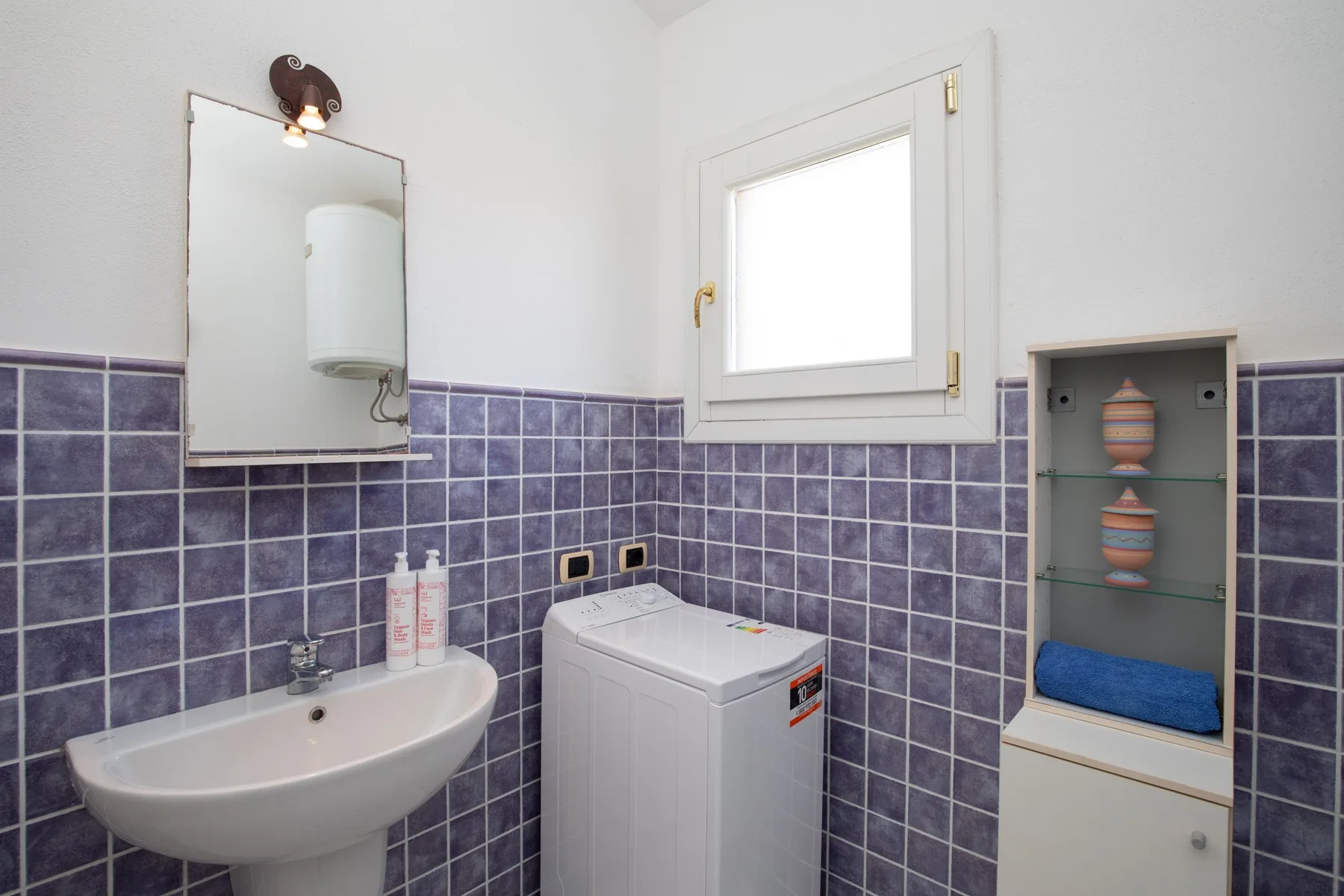 A tiled bathroom with a sink, washing machine, and small wall cabinet.