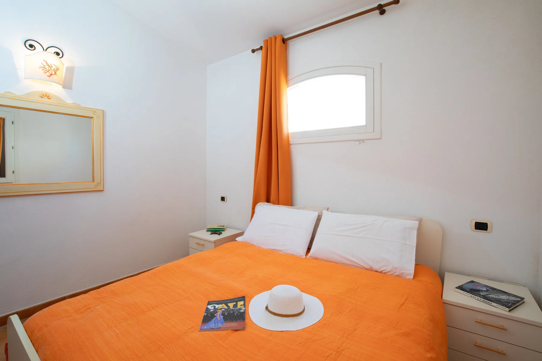 A bedroom with an orange bedspread, white pillows, and a curtained window.