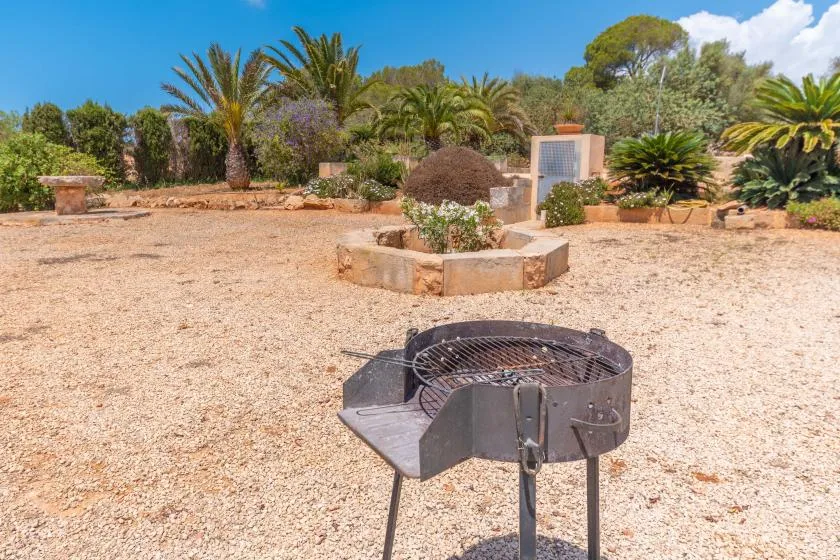 A gravel garden features a metal fire pit in the foreground and palms beyond.