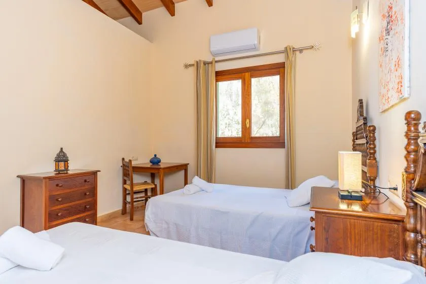 A bedroom with two beds, wooden furnishings, and a window with curtains.