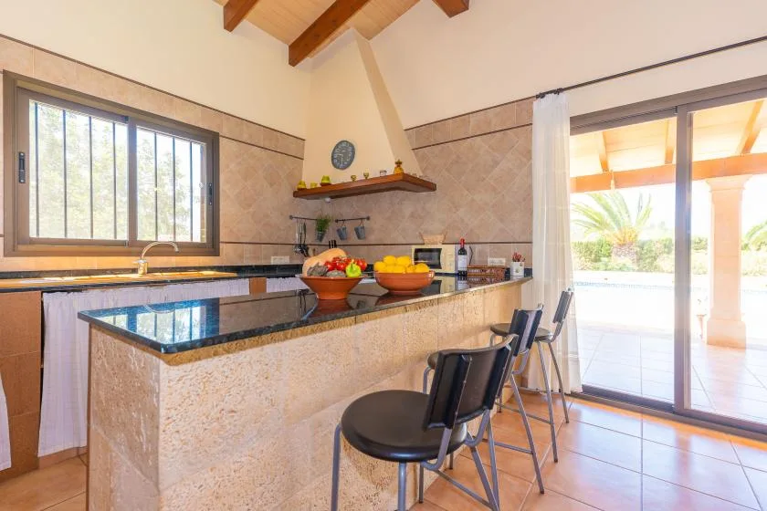 A kitchen with a stone island and bar seating beneath exposed wooden beams.