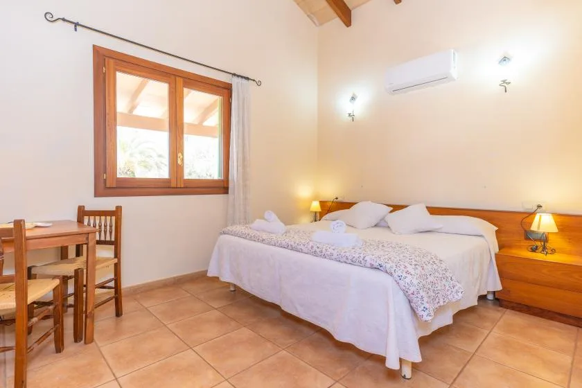A bedroom with a double bed, bedside lamps, and a wooden dining table.