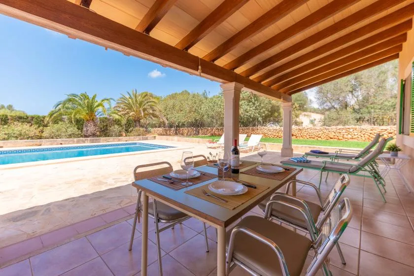 A covered patio dining area overlooks a swimming pool and surrounding greenery.