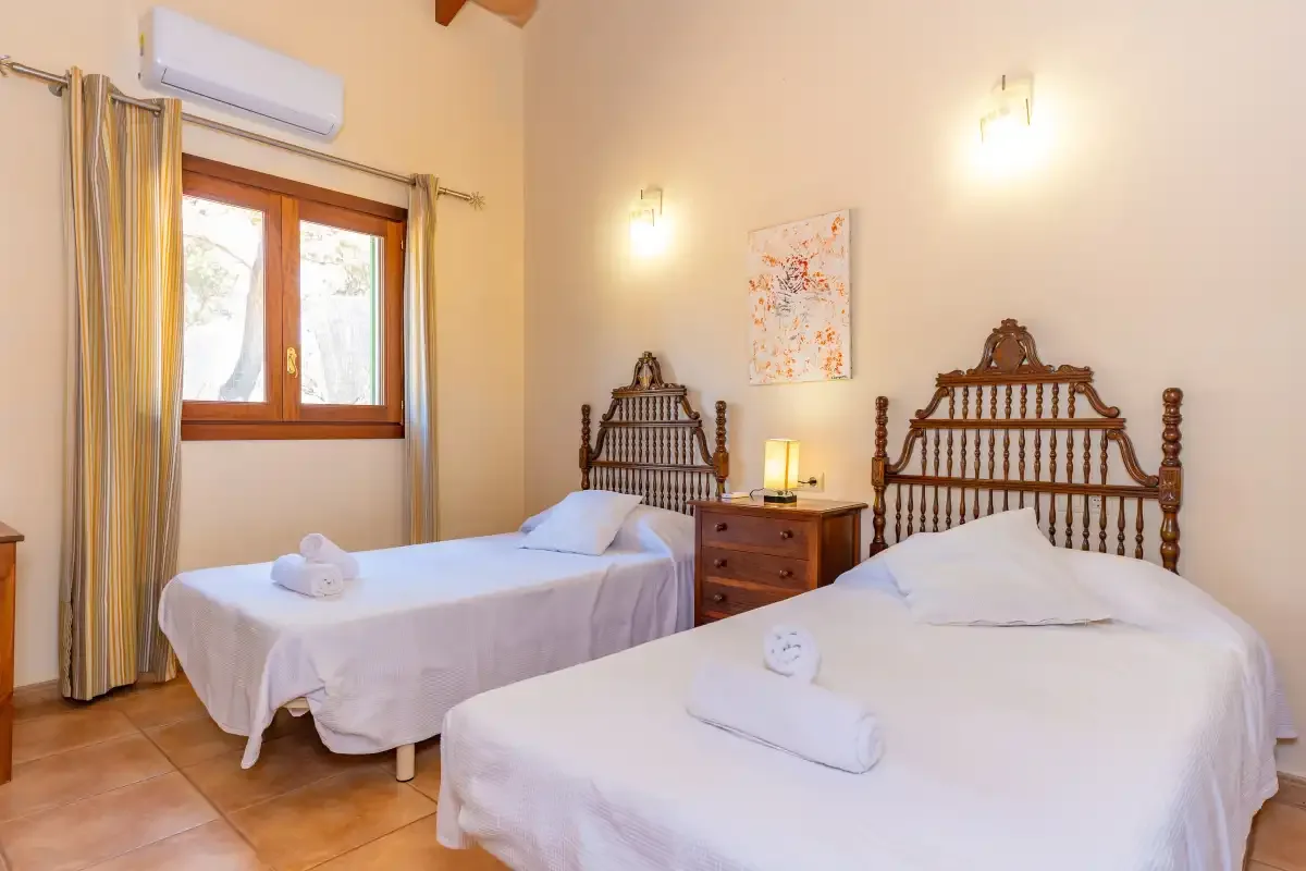 A bedroom with two beds, a wooden bedside table, and a window.