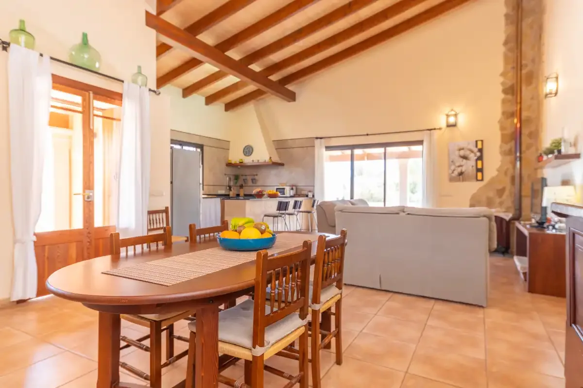 A bright open-plan living and dining area with a kitchen and exposed wooden ceiling beams.