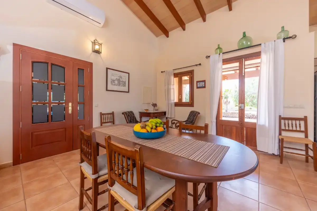 A dining room with a large wooden table and chairs beneath exposed ceiling beams.