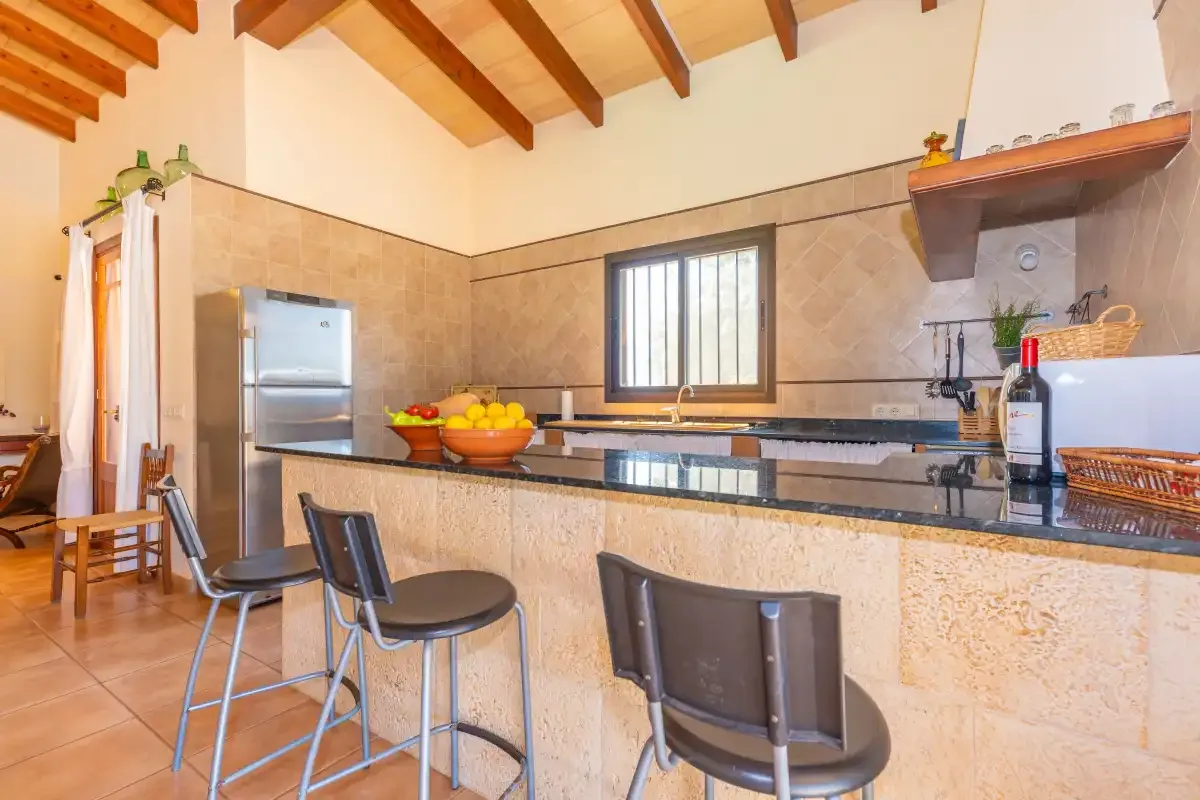 A kitchen with a long counter, bar seating, and exposed ceiling beams.