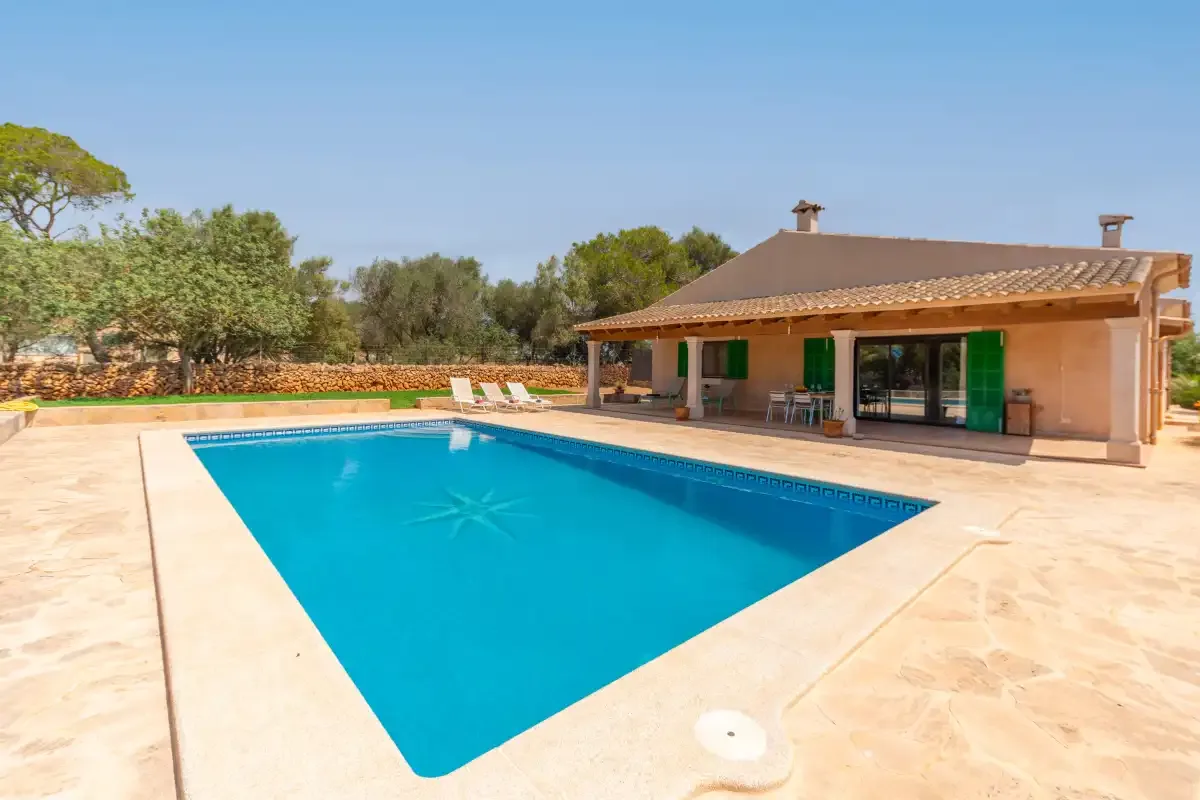 A swimming pool sits beside a single-story house with a covered patio.