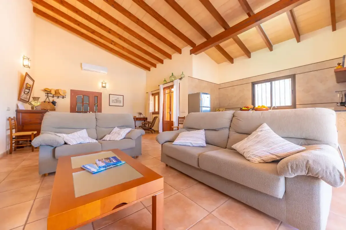 A living room with cushioned seating and a wooden coffee table beneath exposed ceiling beams.
