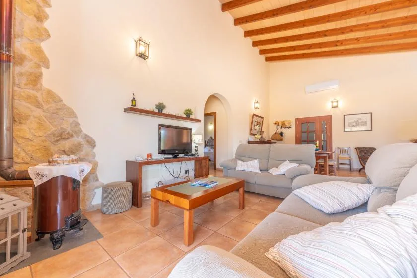 A living room with sofas, a television, and exposed wooden ceiling beams.