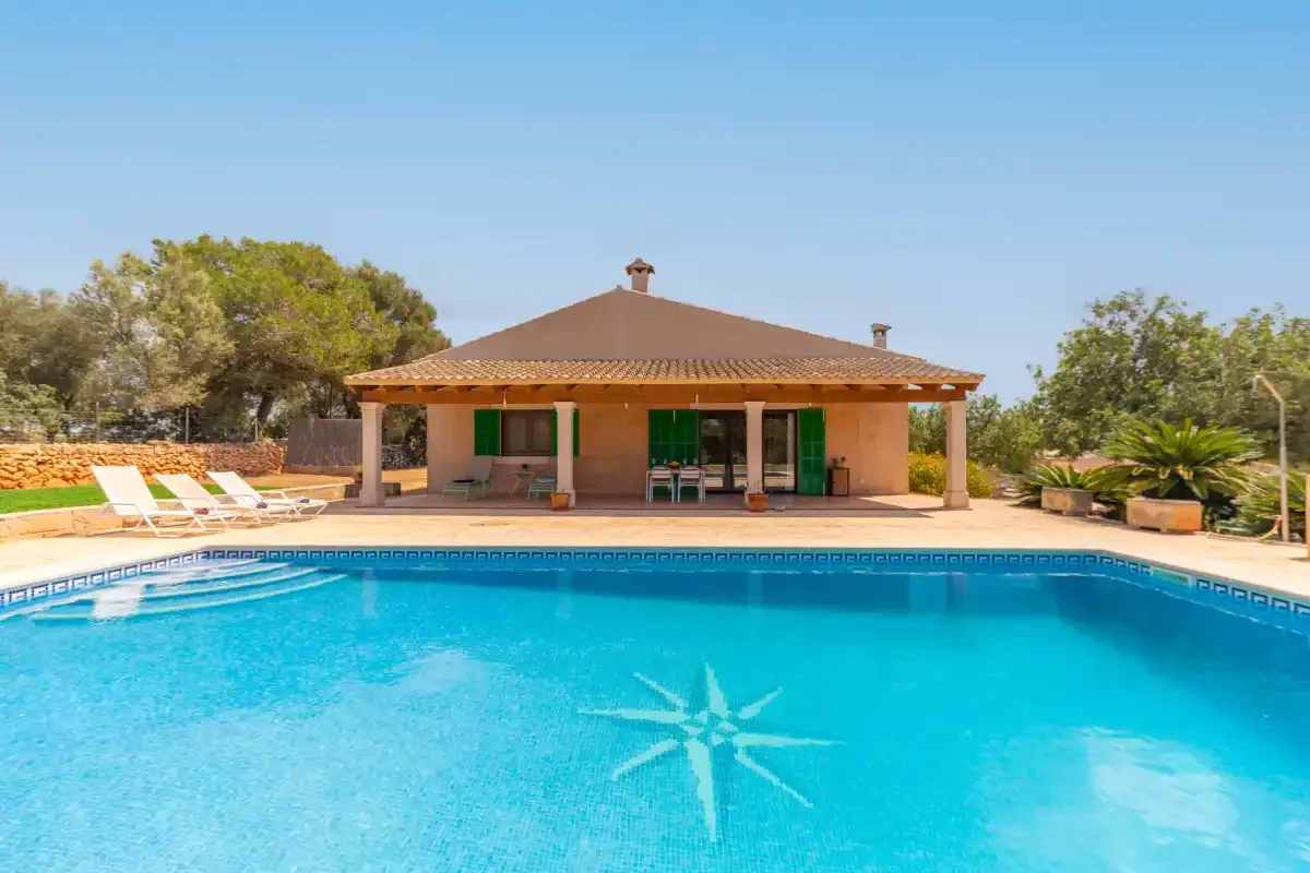 A swimming pool in front of a single-story house with a tiled roof.