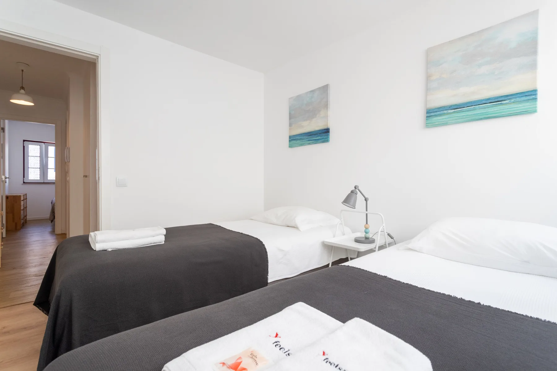 Dormitorio con dos camas, ropa de cama blanca y cuadros de temática costera en las paredes.