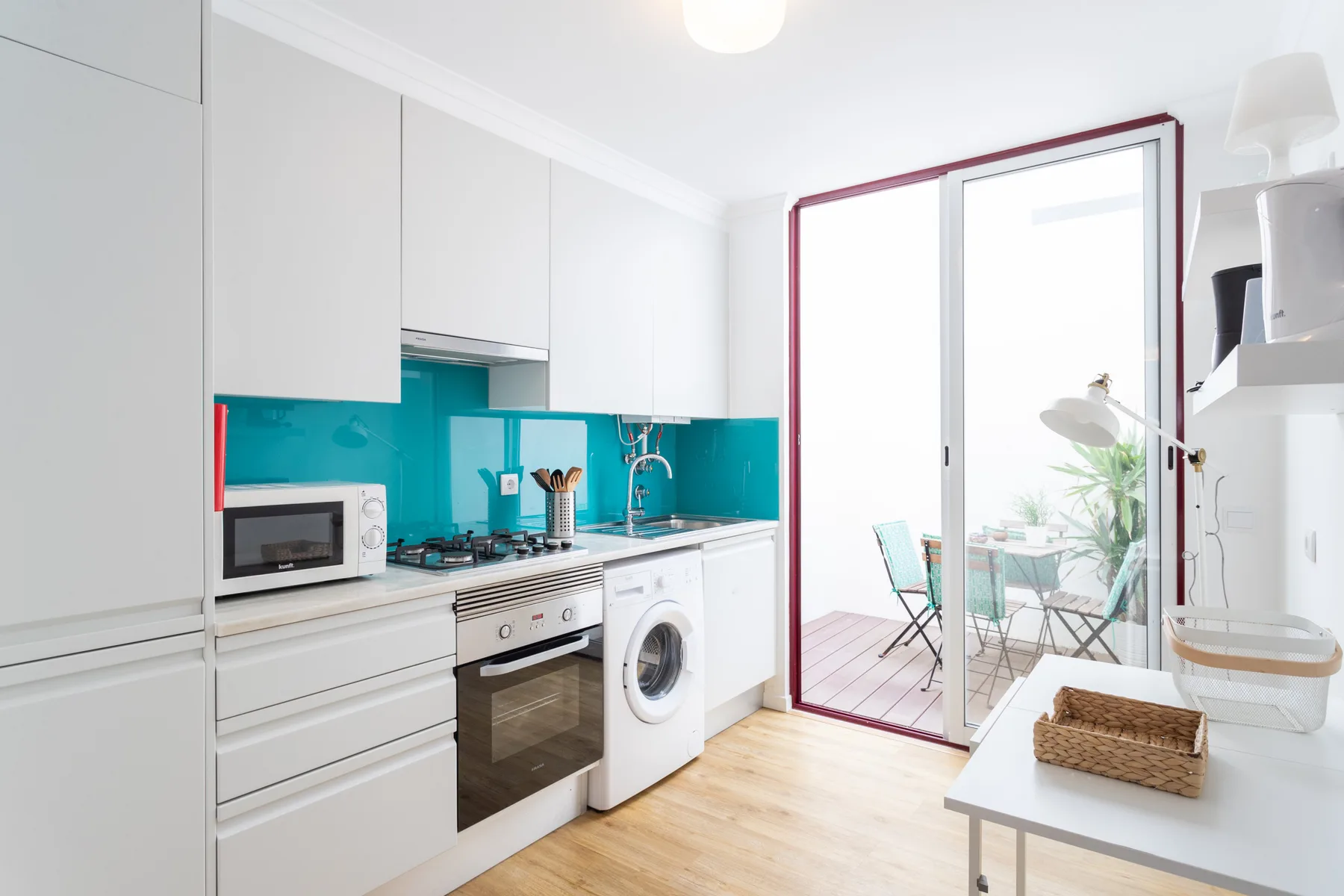 Una cocina luminosa con armarios blancos y puertas de cristal que dan a un balcón.