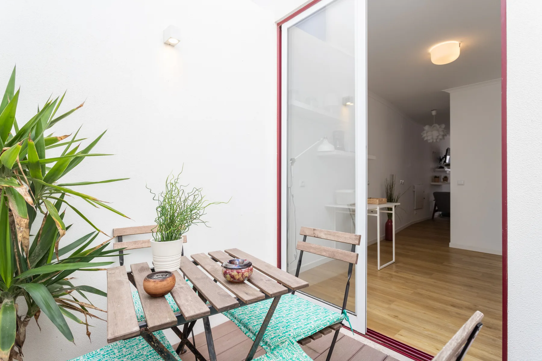 Un pequeño patio con una mesa y sillas de madera está junto a una puerta abierta.