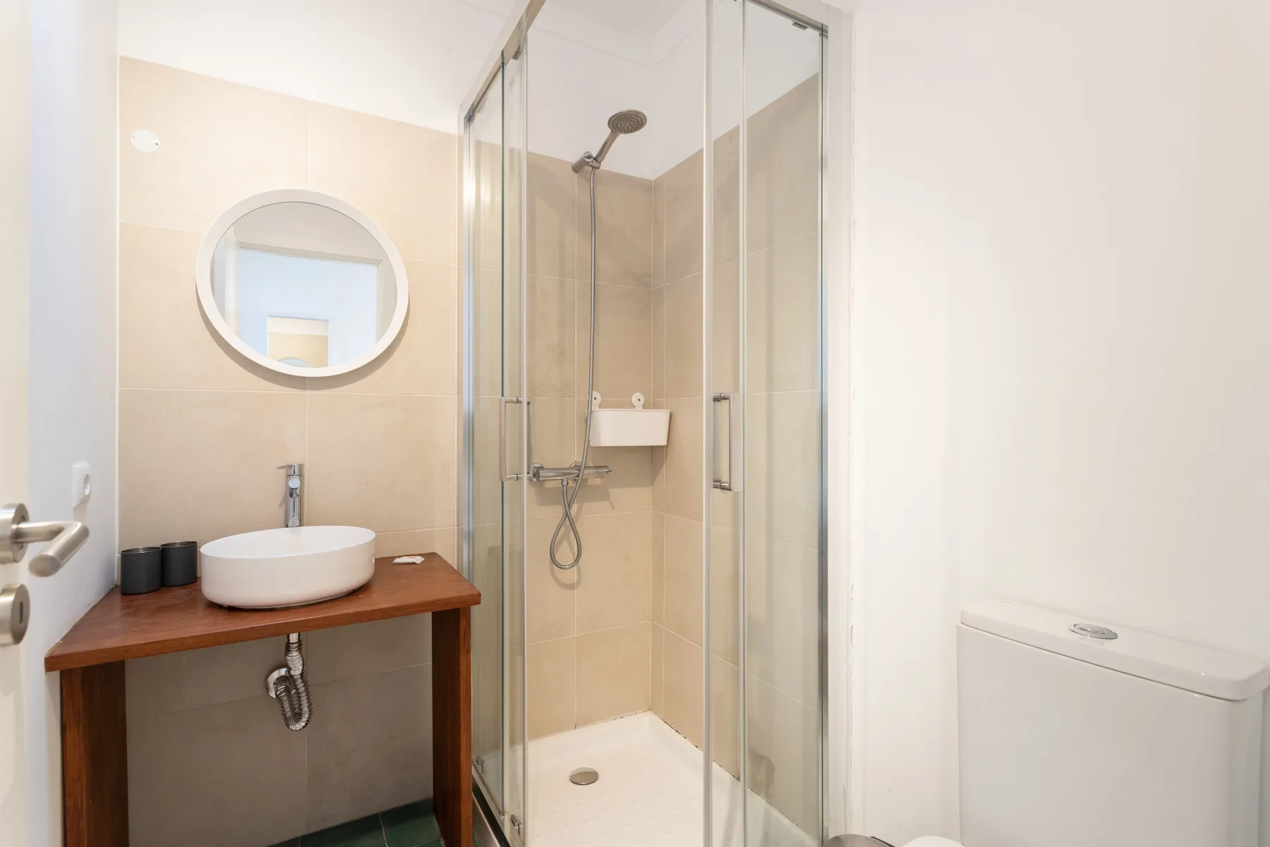Un baño con lavabo, espejo redondo y ducha con mampara de vidrio.