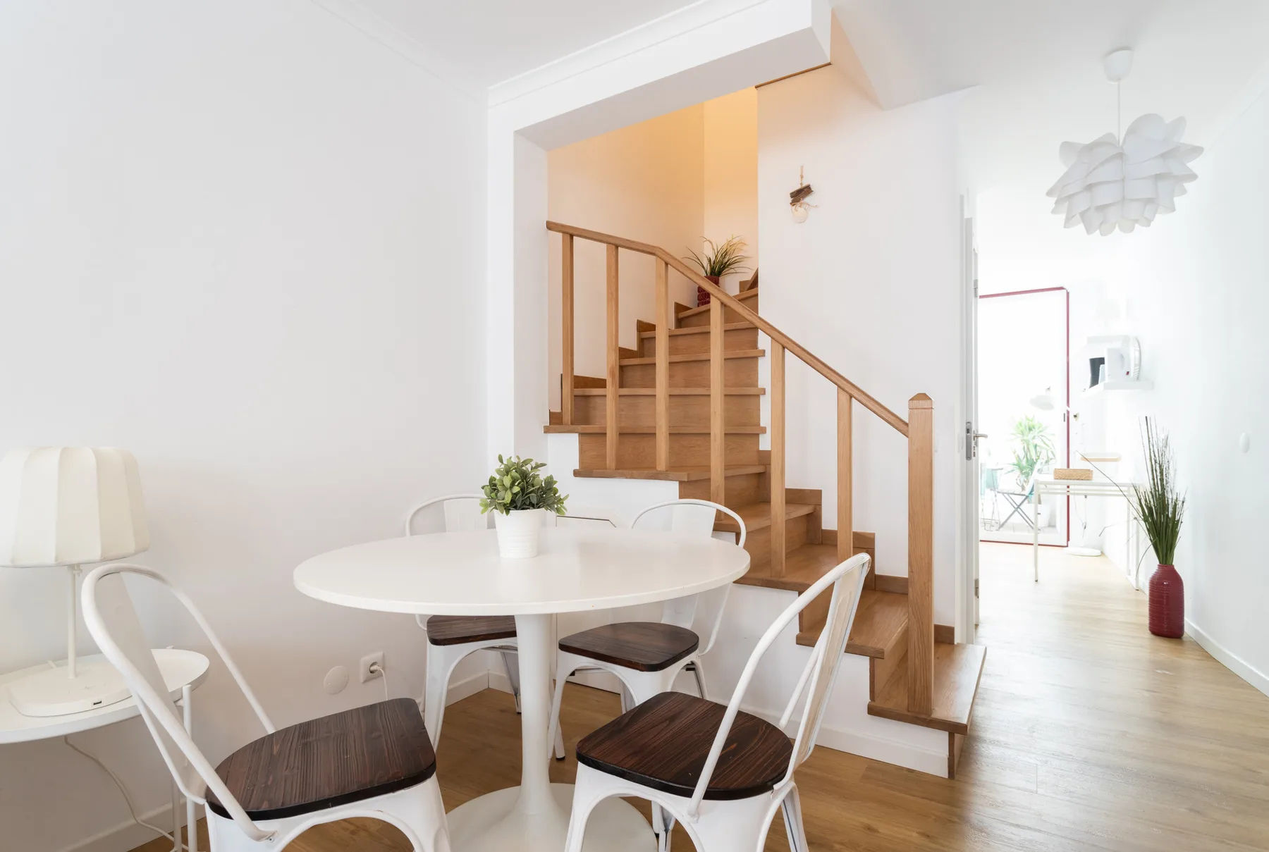 Un comedor luminoso con una mesa redonda junto a una escalera de madera.