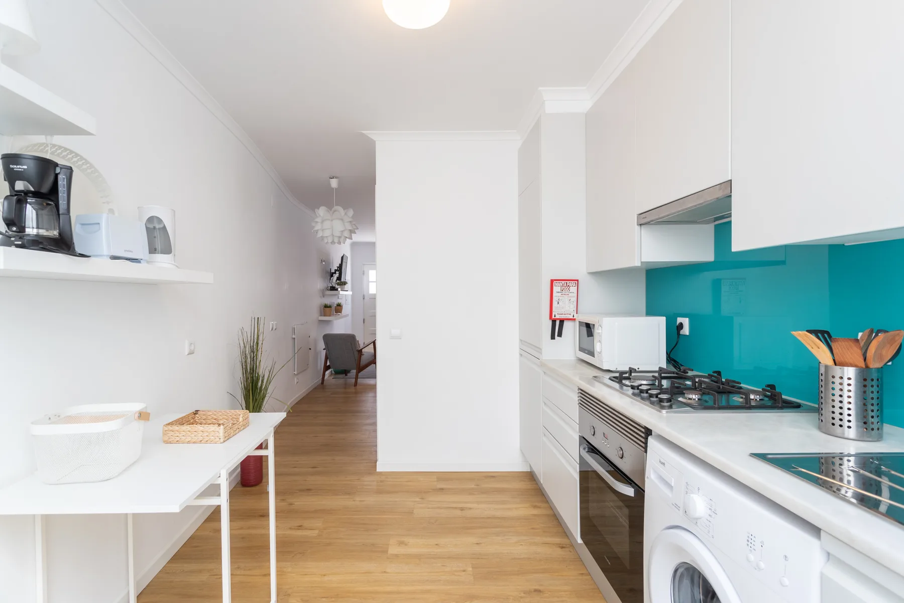 Una cocina luminosa con armarios blancos y un salpicadero turquesa.