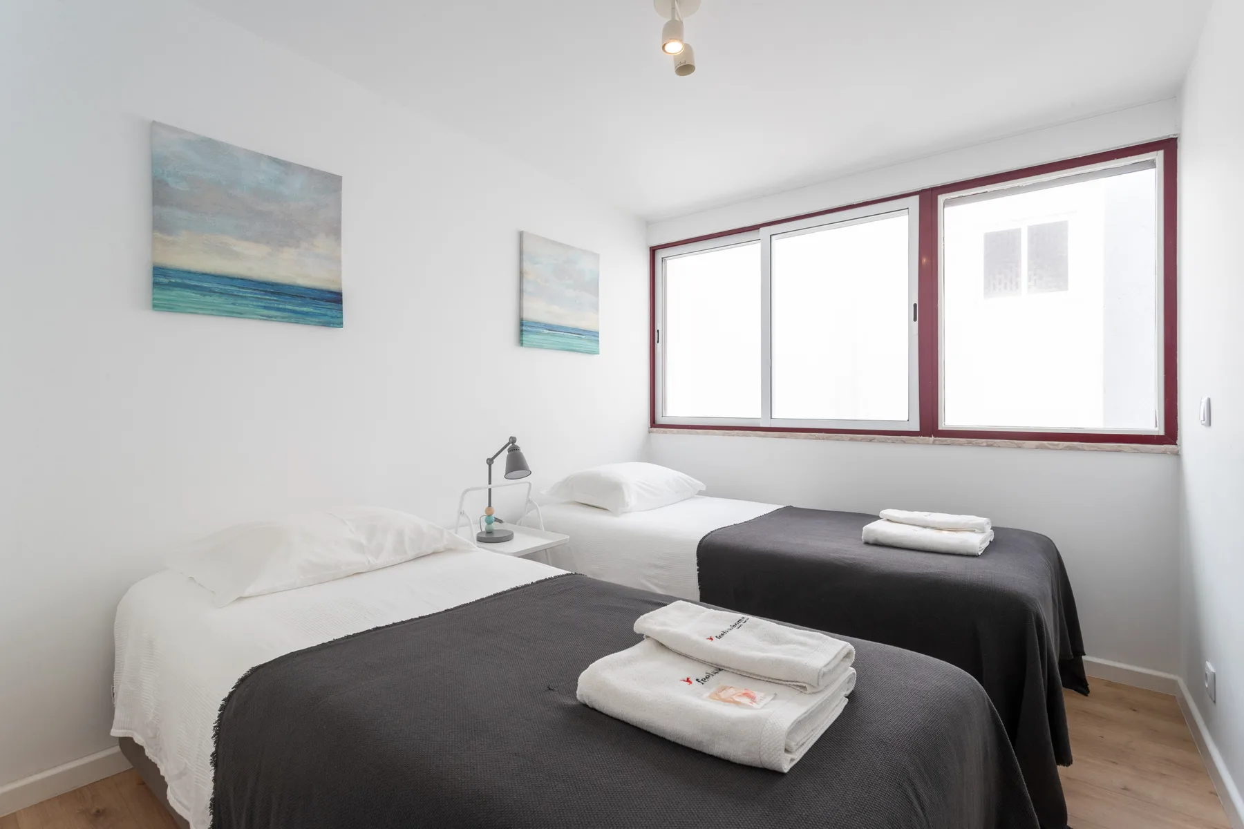 Un dormitorio luminoso con dos camas y ventanas grandes.