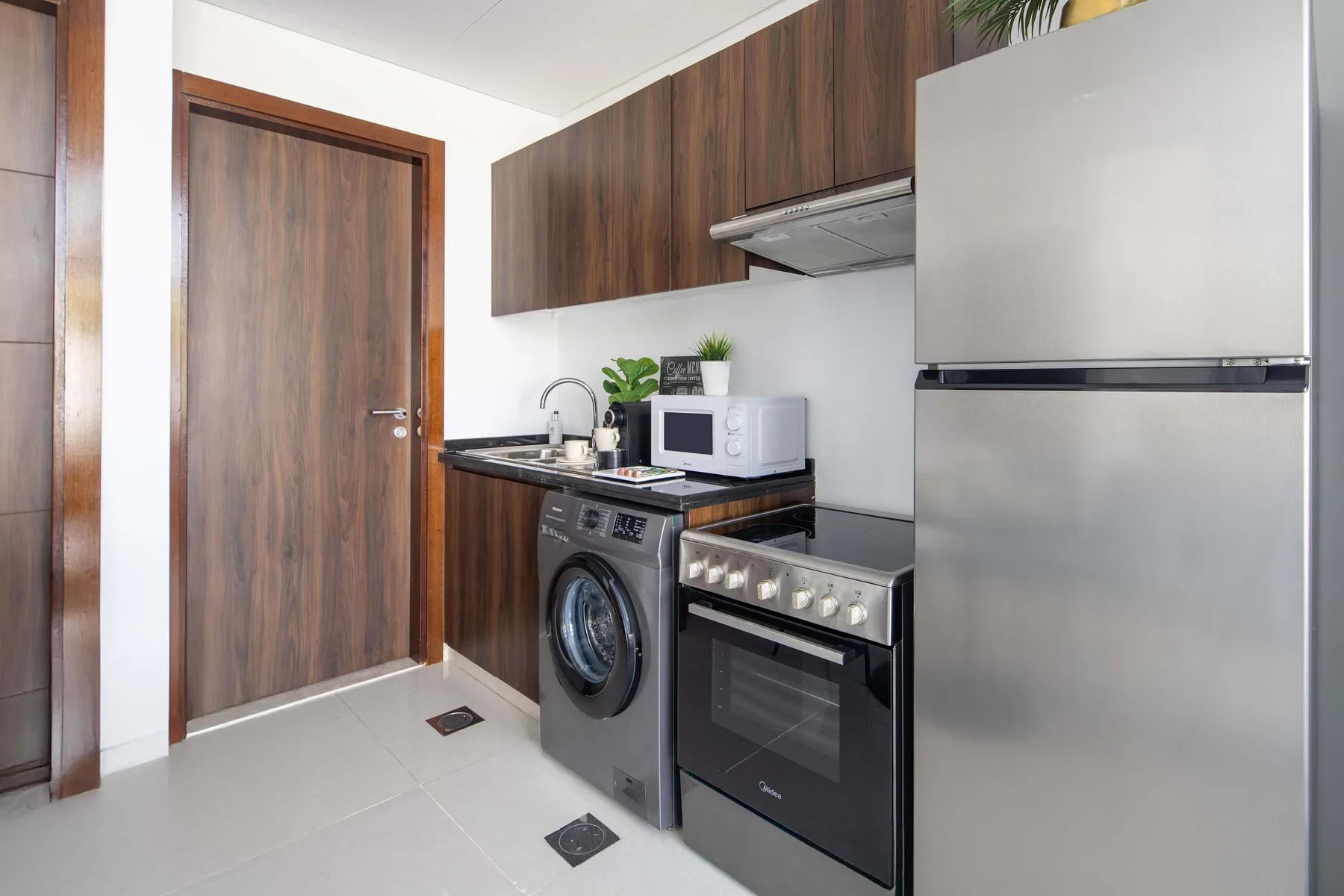 Una cocina compacta con armarios de madera oscura, un refrigerador y una lavadora.