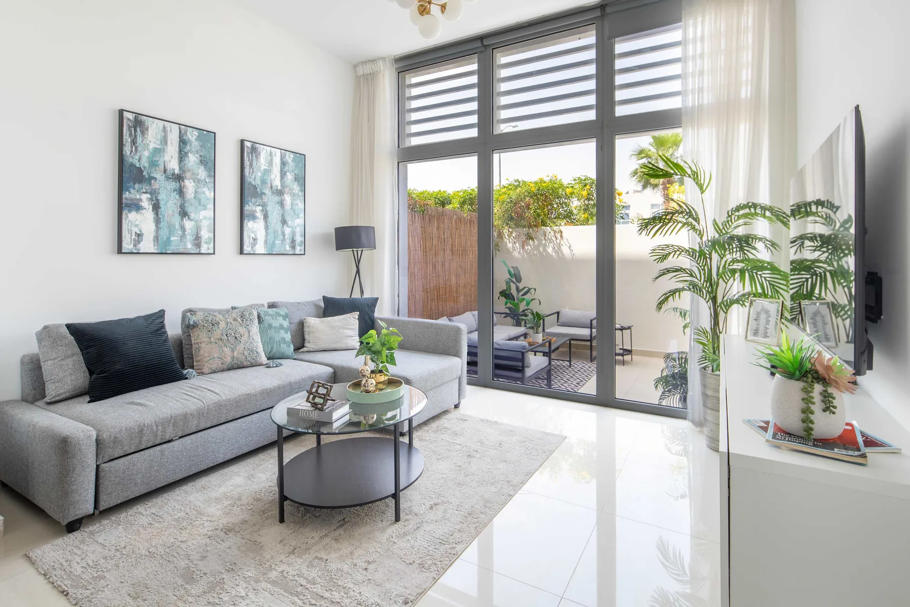 Sala de estar con sofá y grandes ventanales hacia un patio.
