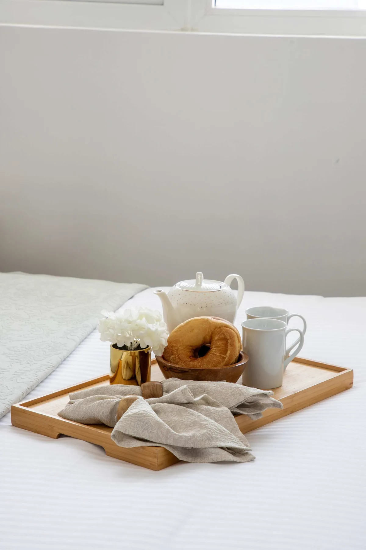 Una bandeja de desayuno con té, un bagel y flores está sobre una cama.