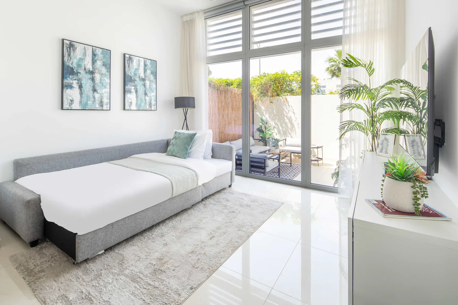 Un dormitorio luminoso con una cama bien tendida y grandes ventanas que dan a un patio.