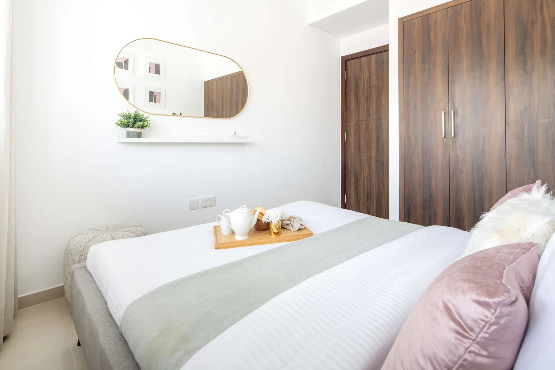 Un dormitorio luminoso con una cama tendida y un armario de madera.