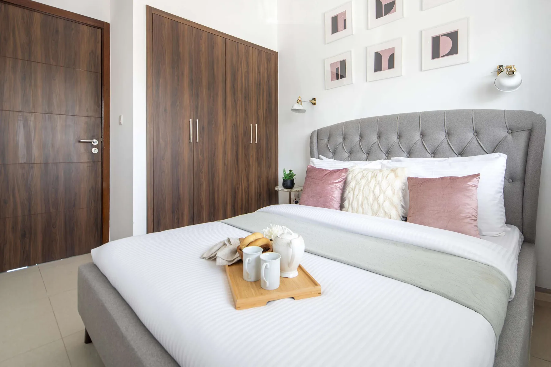 Un dormitorio luminoso con una cama bien tendida y un cabecero tapizado.