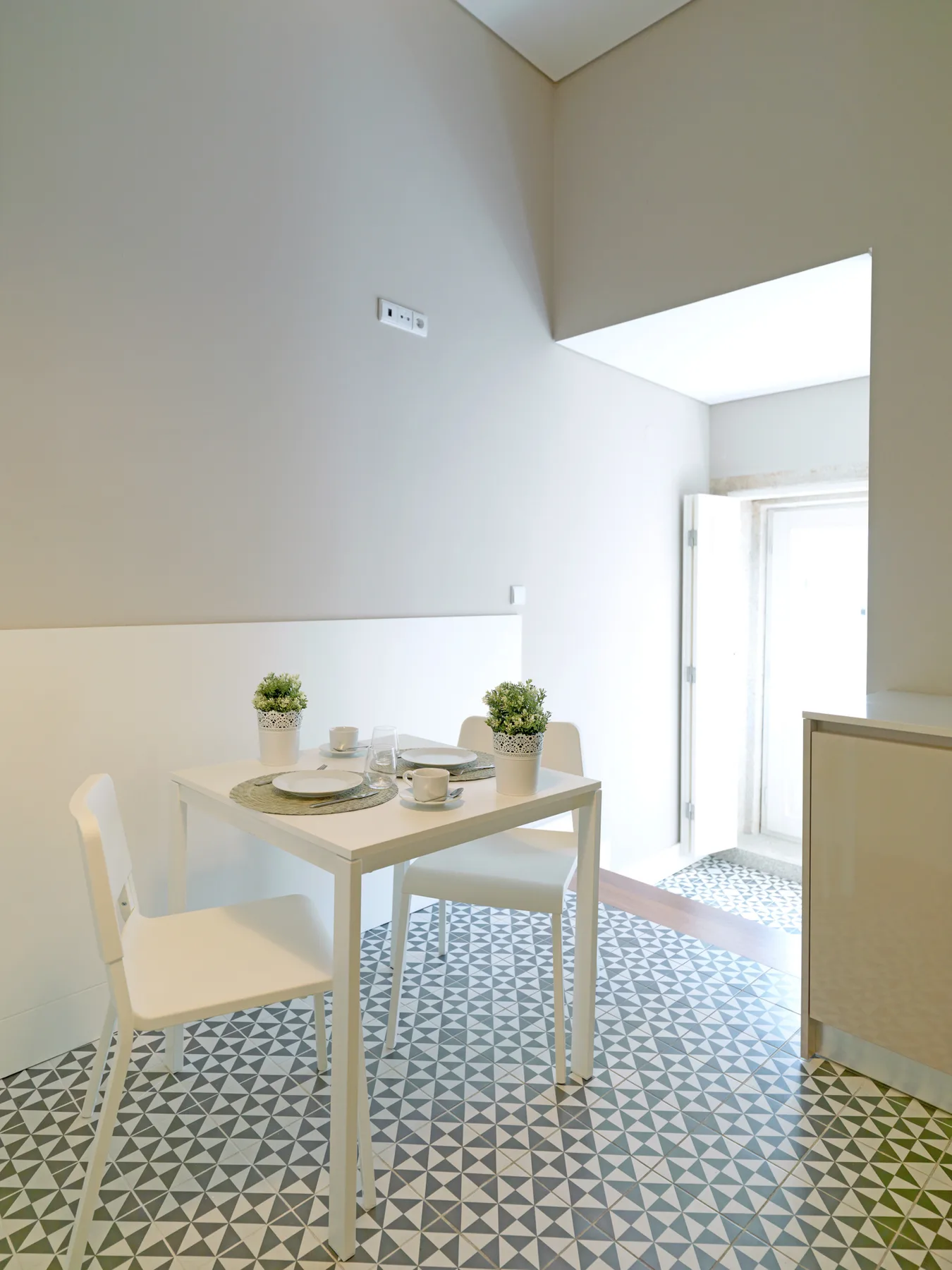 A bright dining area with a table, seating, and patterned floor tiles.