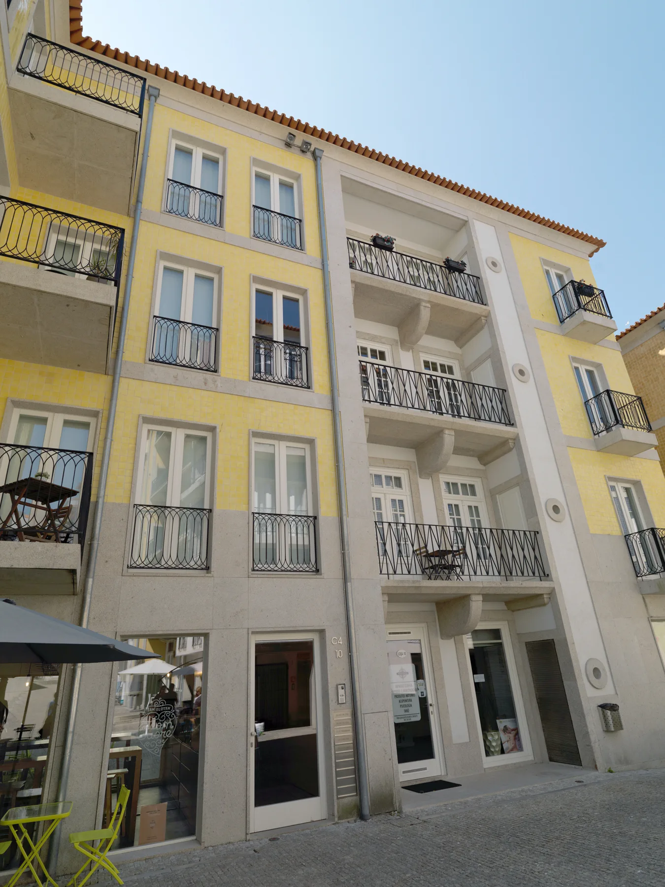 Street view of a multi-story building with balconies and ground-floor storefronts.