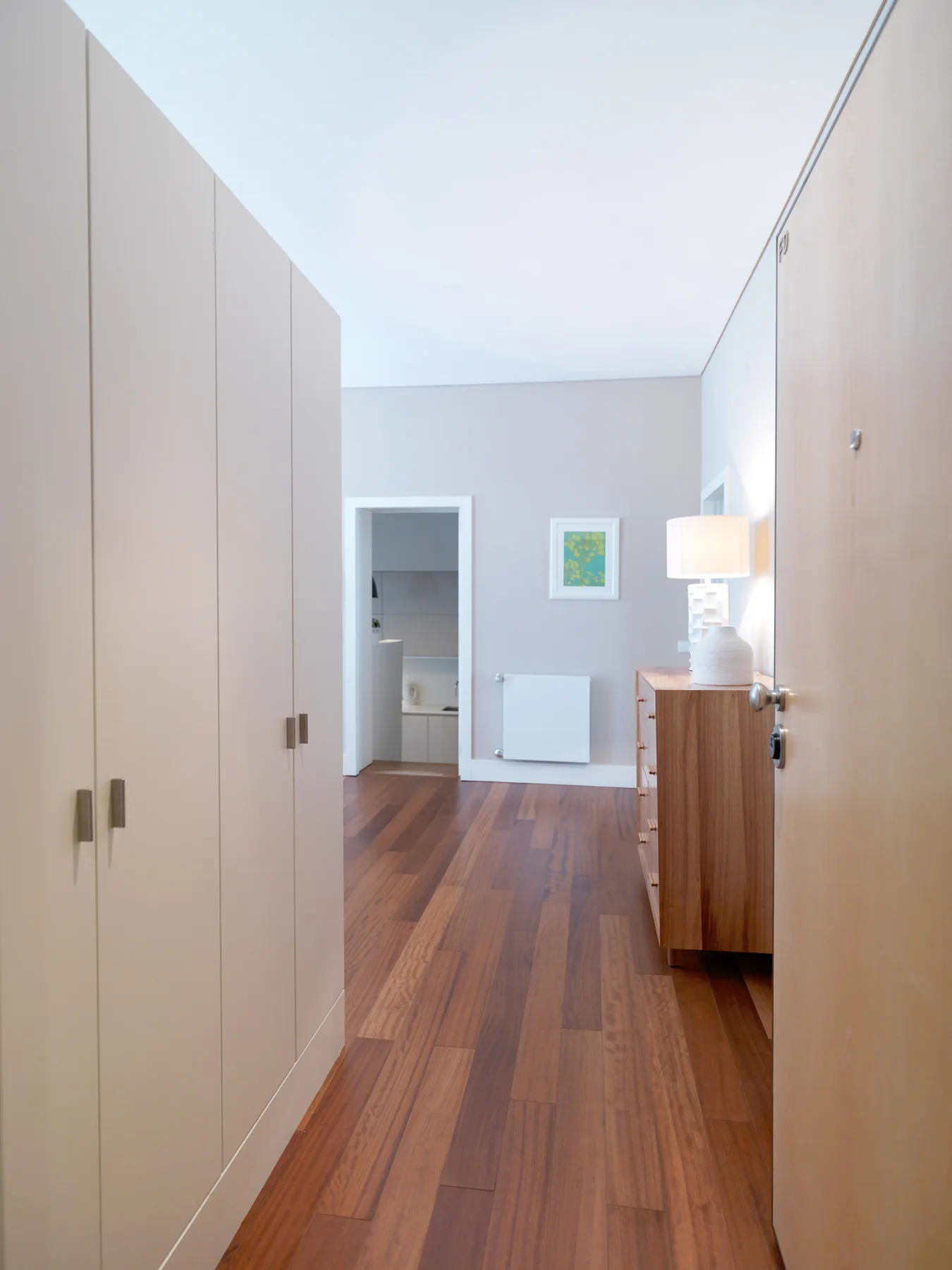 A hallway with built-in cabinets, wood flooring, and a doorway at the far end.
