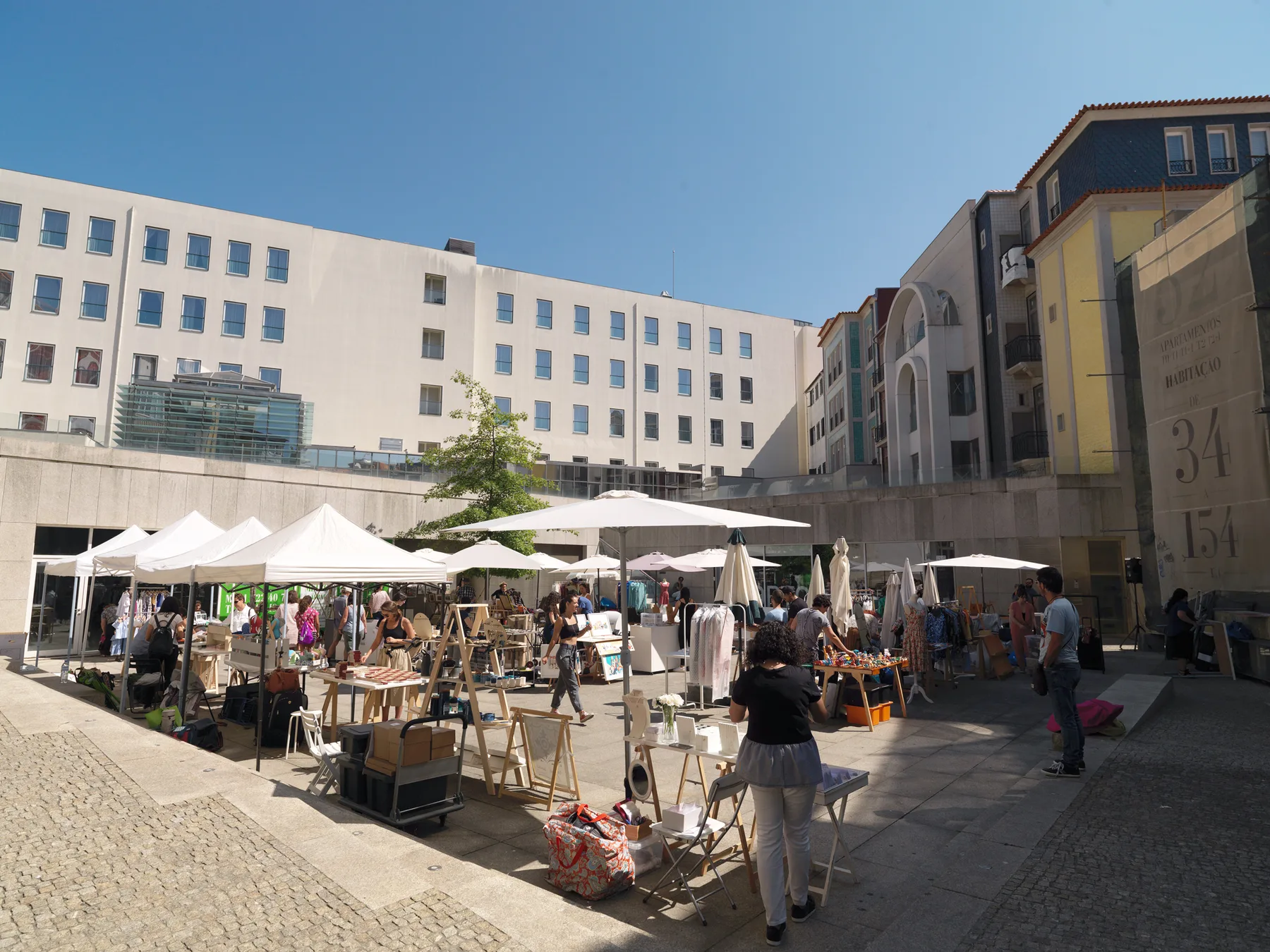 An outdoor market fills a paved plaza beneath surrounding city buildings.