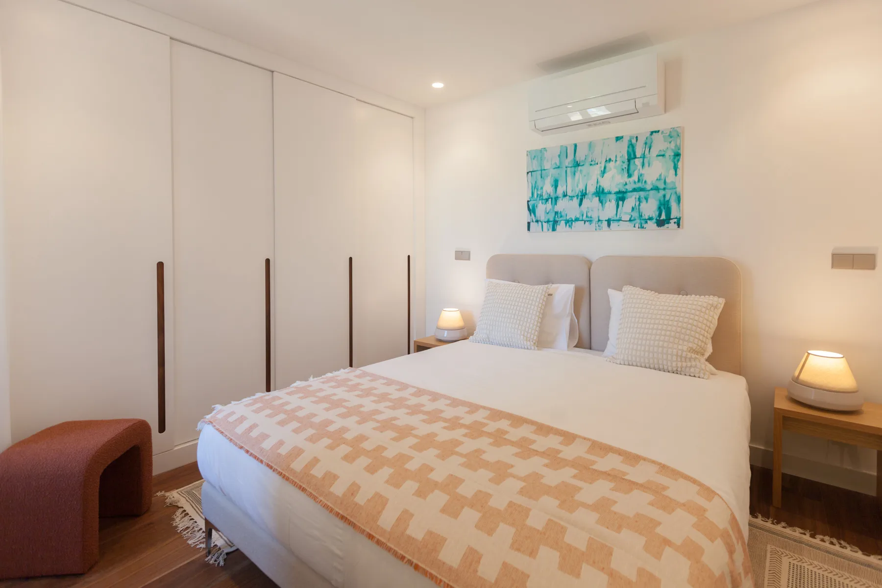 A bedroom with a double bed, patterned bedding, and a colorful artwork above the headboard.