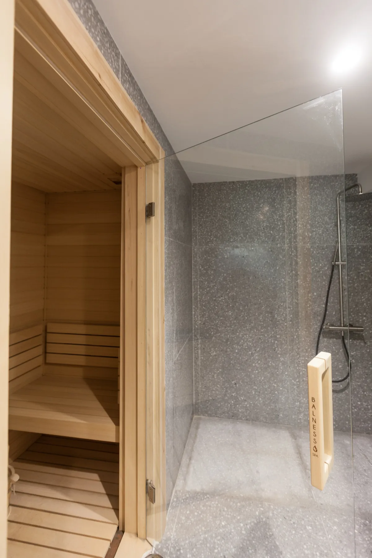 Un baño con una sauna de madera junto a una ducha alicatada.