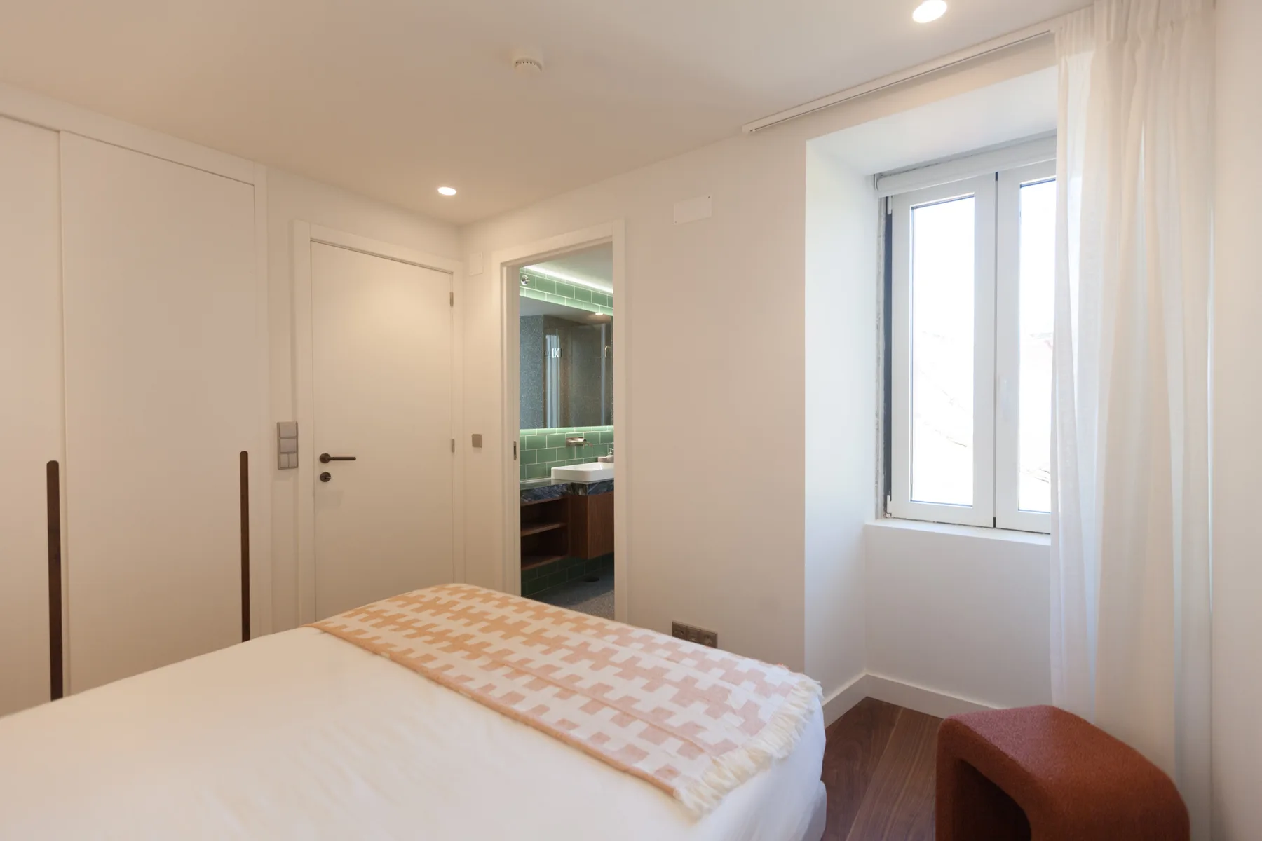 Dormitorio con una cama junto a una ventana luminosa y una puerta abierta.