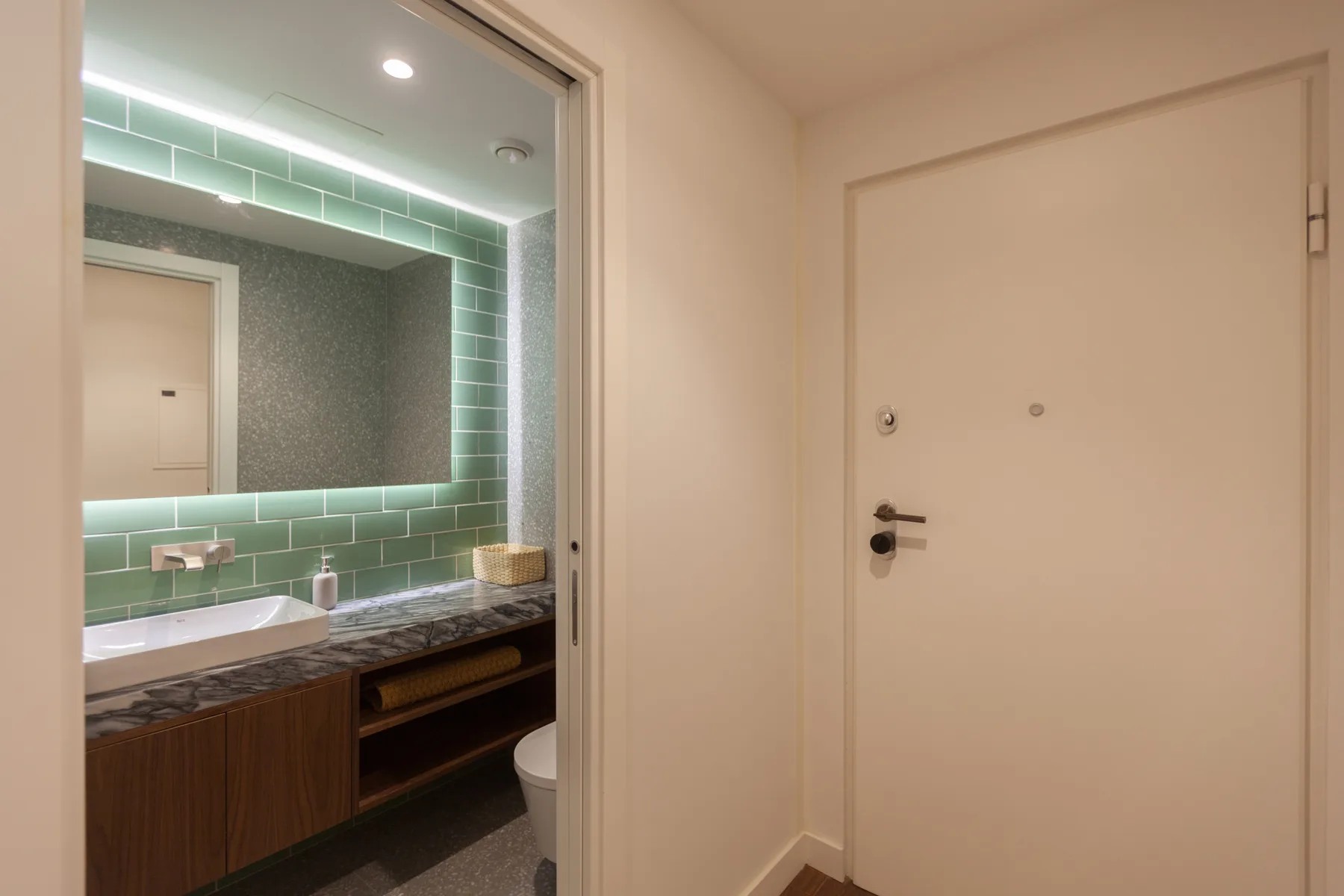 A bathroom vanity with a wide mirror is visible beside a closed interior door.