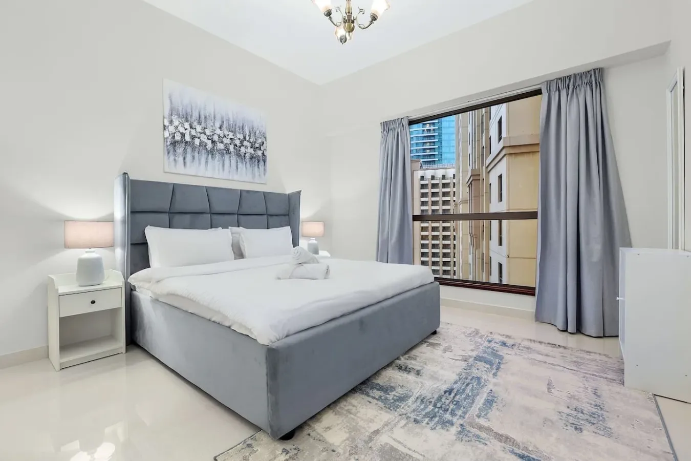 A bedroom with a gray bed beside a large curtained window.